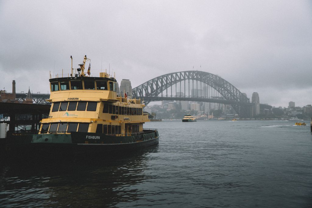 The yellow-and-green Sydney ferry Fishburn moored at Circular Quay, with the Harbour Bridge in grey haze behind.